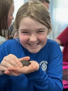 A smiling Mayflower student holding a small classroom animal
